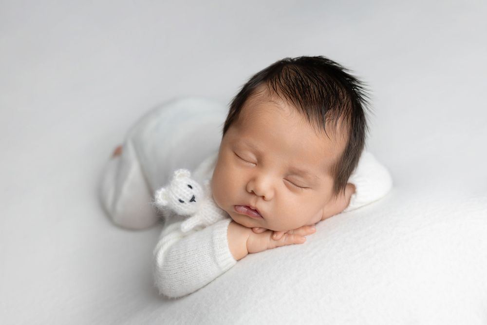 Newborn baby in white with small white bear, taken by Jen Knightstep, Photographer
