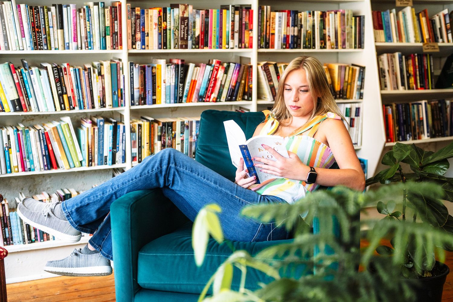 A cozy reading nook with white bookshelves filled with colorful books and a comfortable blue couch by the window.