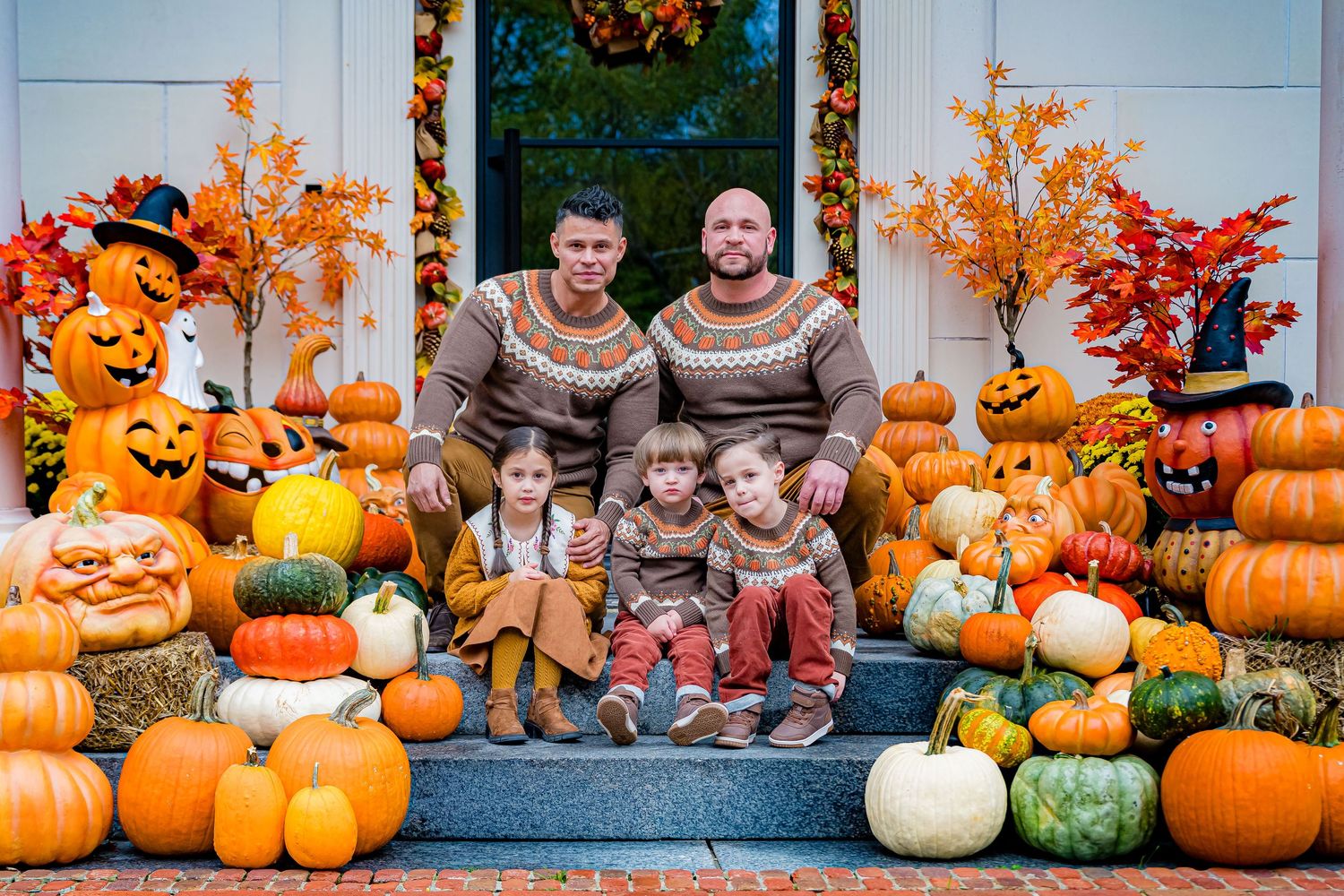 A festive autumn display of orange pumpkins, gourds, and fall foliage arranged along a rustic wooden porch railing.