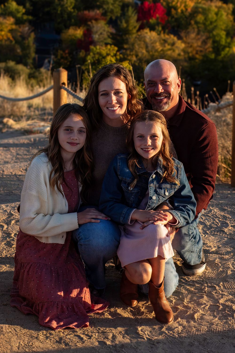 A  portrait showing a group sitting together on sandy ground in warm evening light.