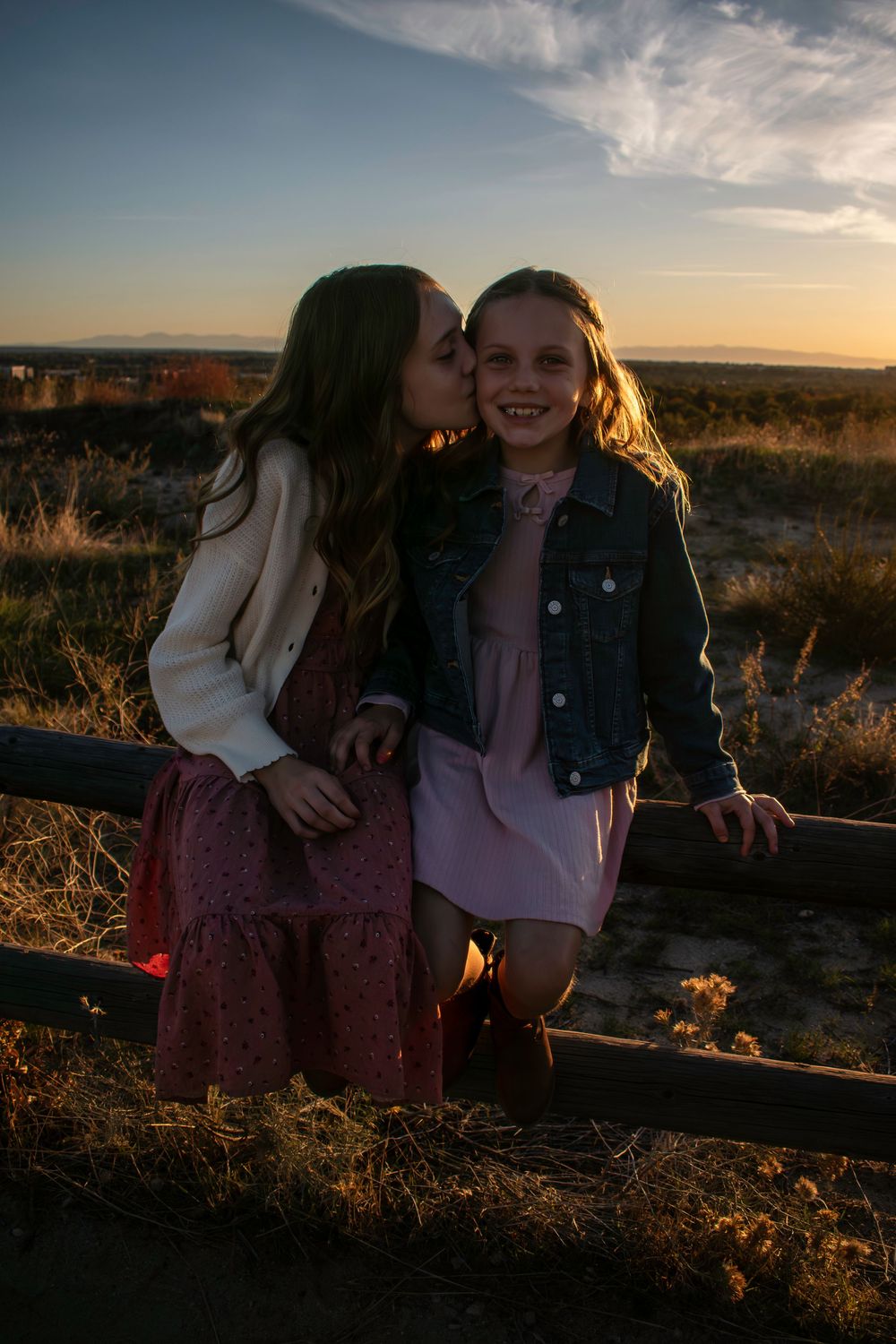 Two sisters at sunset in a grassy field with golden light illuminating the scene.
