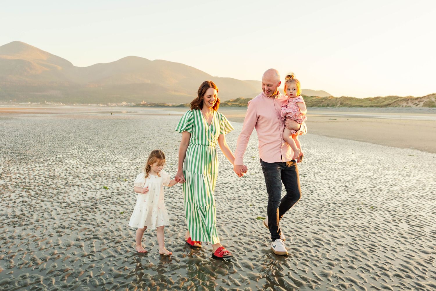 Family walking together on a sandy beach at sunset while holding hands and enjoying quality time together.