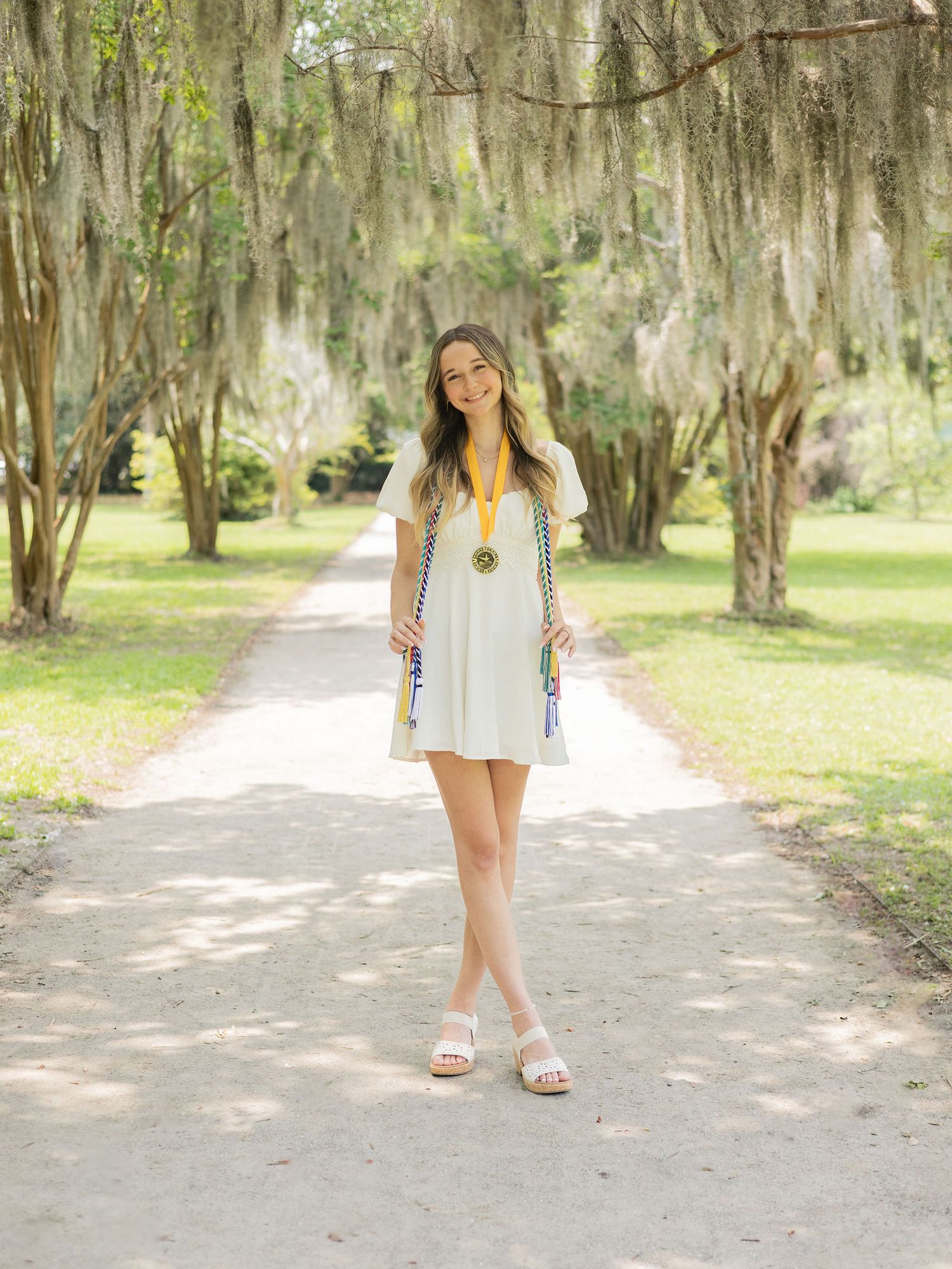 Four connected images show a person in a white dress walking along a scenic path under moss-draped oak trees in a park setting.