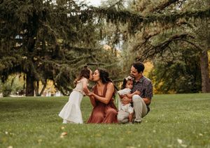 Picnic scene on lush green grass with people relaxing under trees in golden afternoon light.