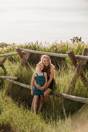 Children sitting on rustic wooden fence in tall summer grass during golden hour photography session.