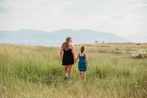 Two people walk together through a serene grassland meadow with mountains visible in the distance.