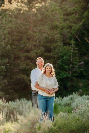 A couple embraces in a romantic outdoor setting with lavender flowers and trees in the background at sunset.