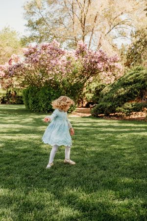 A child in a light blue dress twirls on green grass with blooming cherry trees in the background during spring.