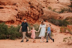 People walking along red rock formations in a desert landscape during sunset.