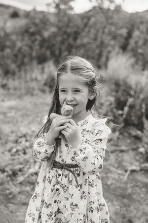 A series of black and white photos showing a child in a floral dress laughing and covering their face outdoors.