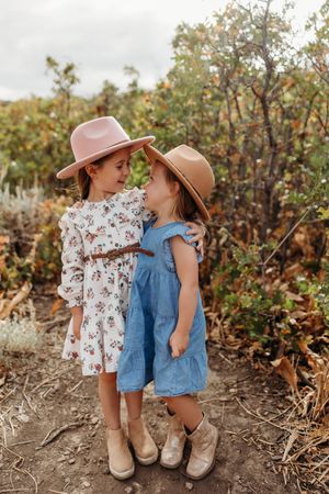 Two young children in sun hats and summer outfits play together in a garden setting during golden hour.