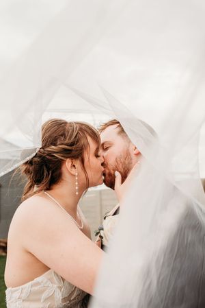 A romantic wedding moment captured under a flowing white veil as the couple shares a tender kiss outdoors.