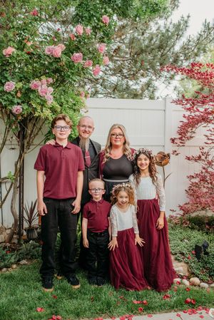 Family wearing coordinated burgundy and white outfits poses together in a garden setting with pink flowers and greenery.