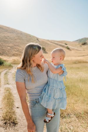 A parent and child share a tender moment together on a dirt path through golden rolling hills on a sunny day.