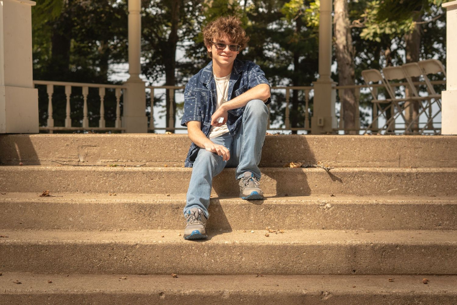 Person in denim sits casually on concrete steps during a sunny day outdoors.