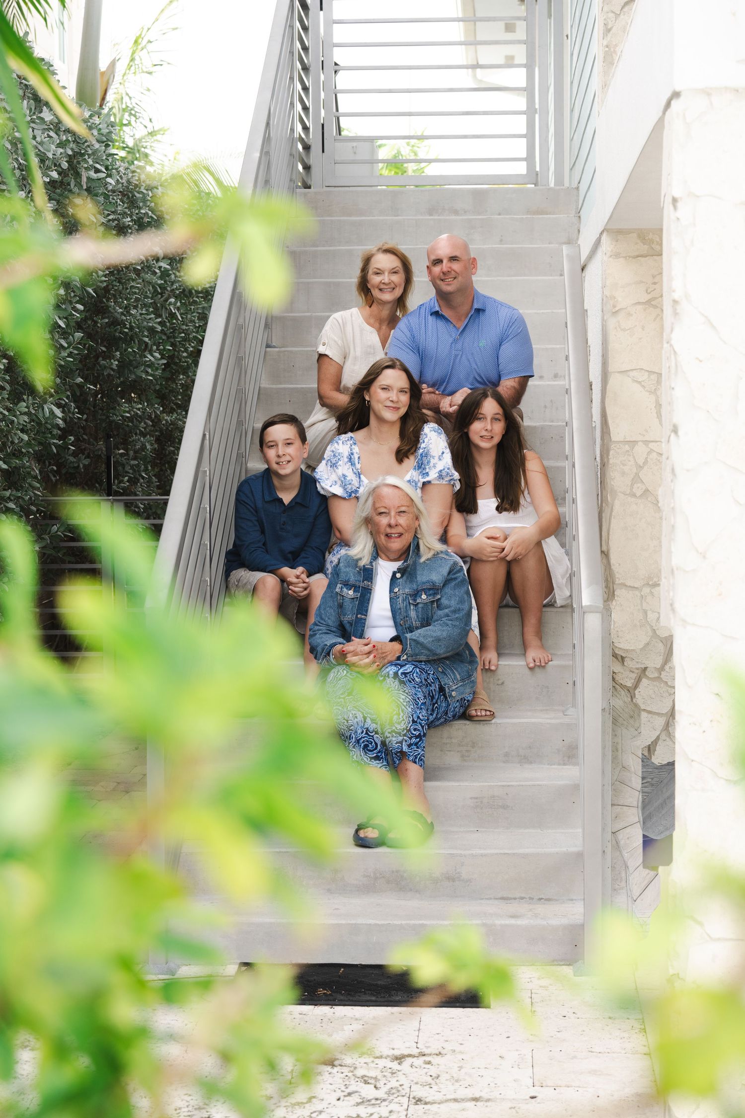 A group of people sit together on outdoor stone steps surrounded by greenery and white columns.