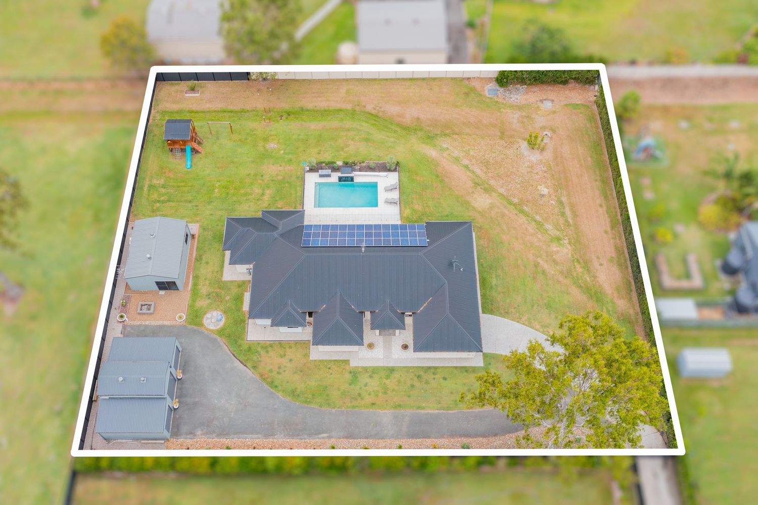 Aerial view of large residential property featuring inground pool, solar panels, and spacious lawns within white boundary.