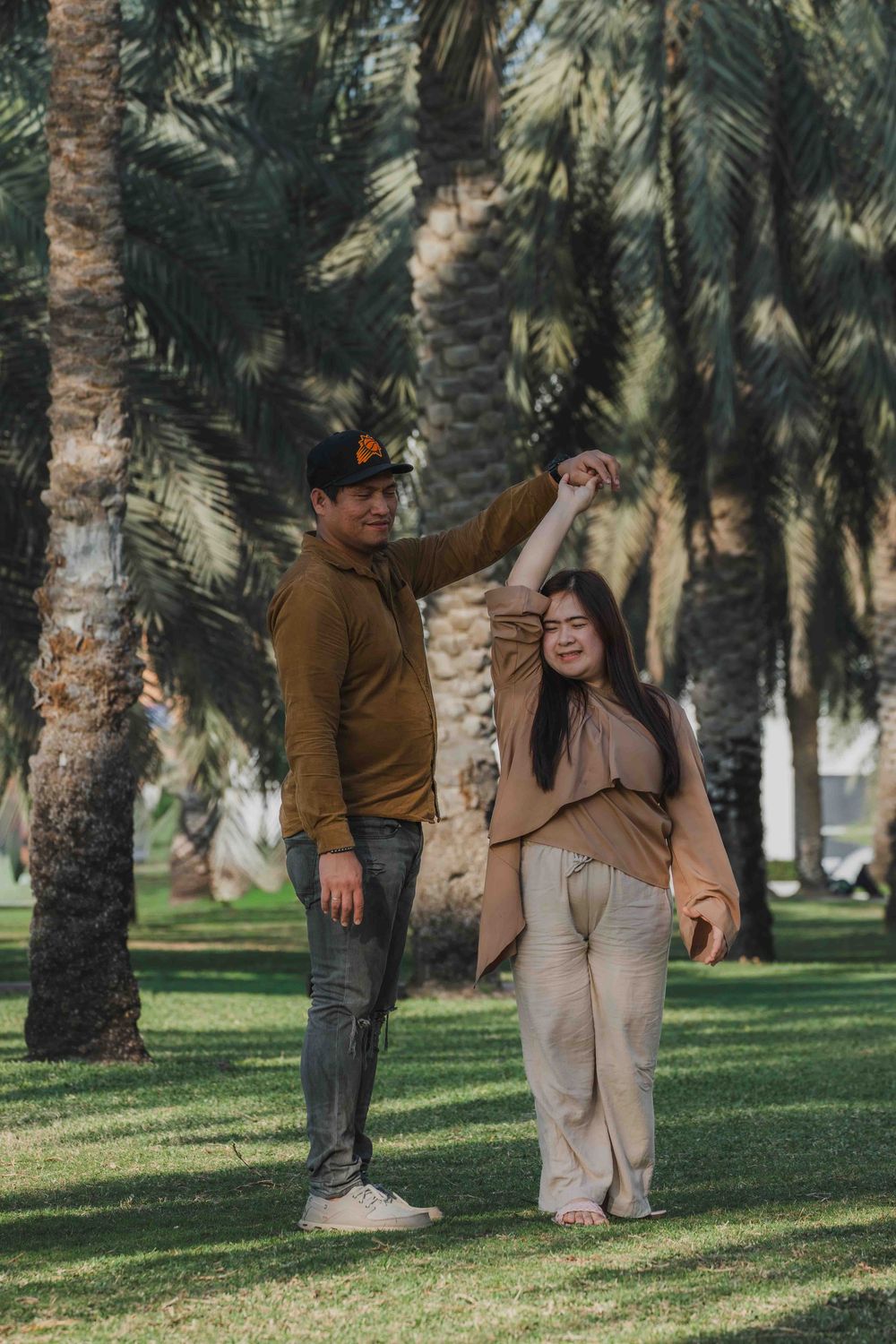 Couple spinning in Abu Dhabi park, palm trees background. Lifestyle Family & Couple Photographer in Abu Dhabi.
