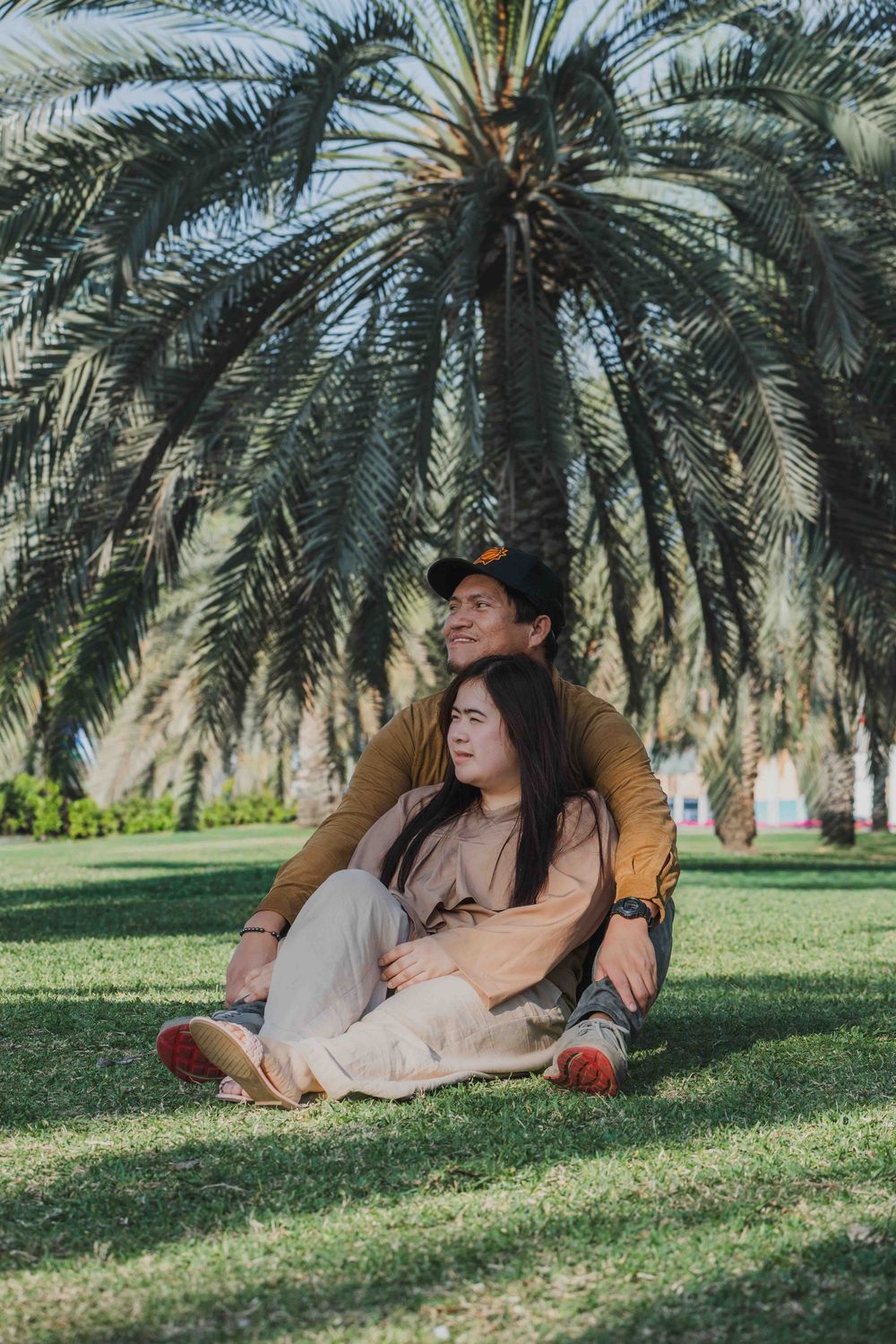 Couple sitting in Abu Dhabi park, palm trees background. Lifestyle Family & Couple Photographer in Abu Dhabi.