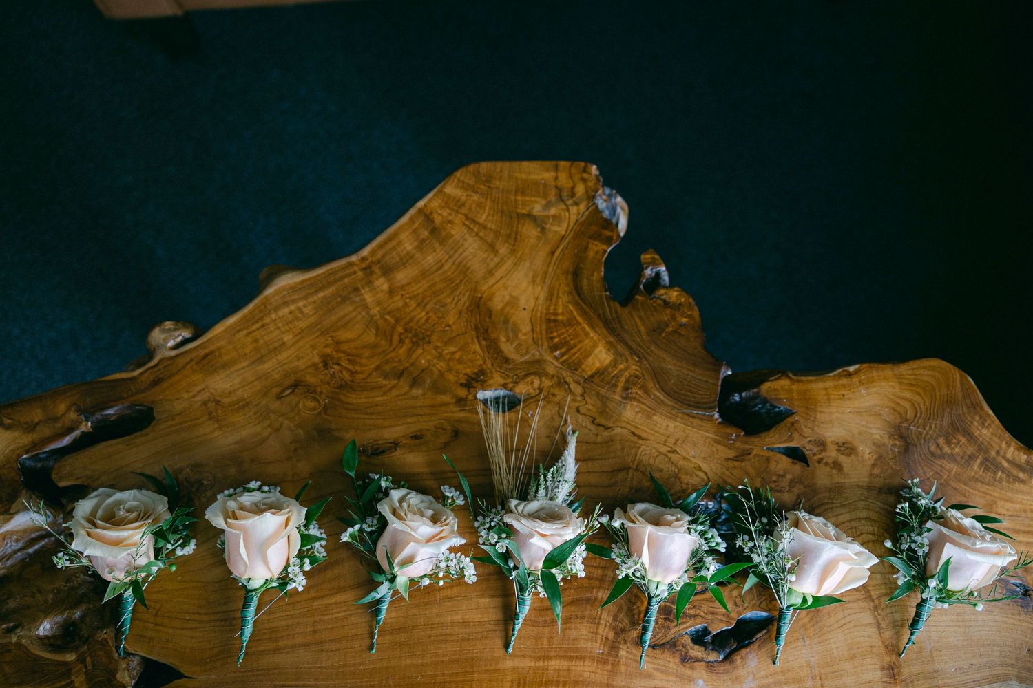 A row of rustic wooden tables decorated with small white floral centerpieces and mint green ribbons.