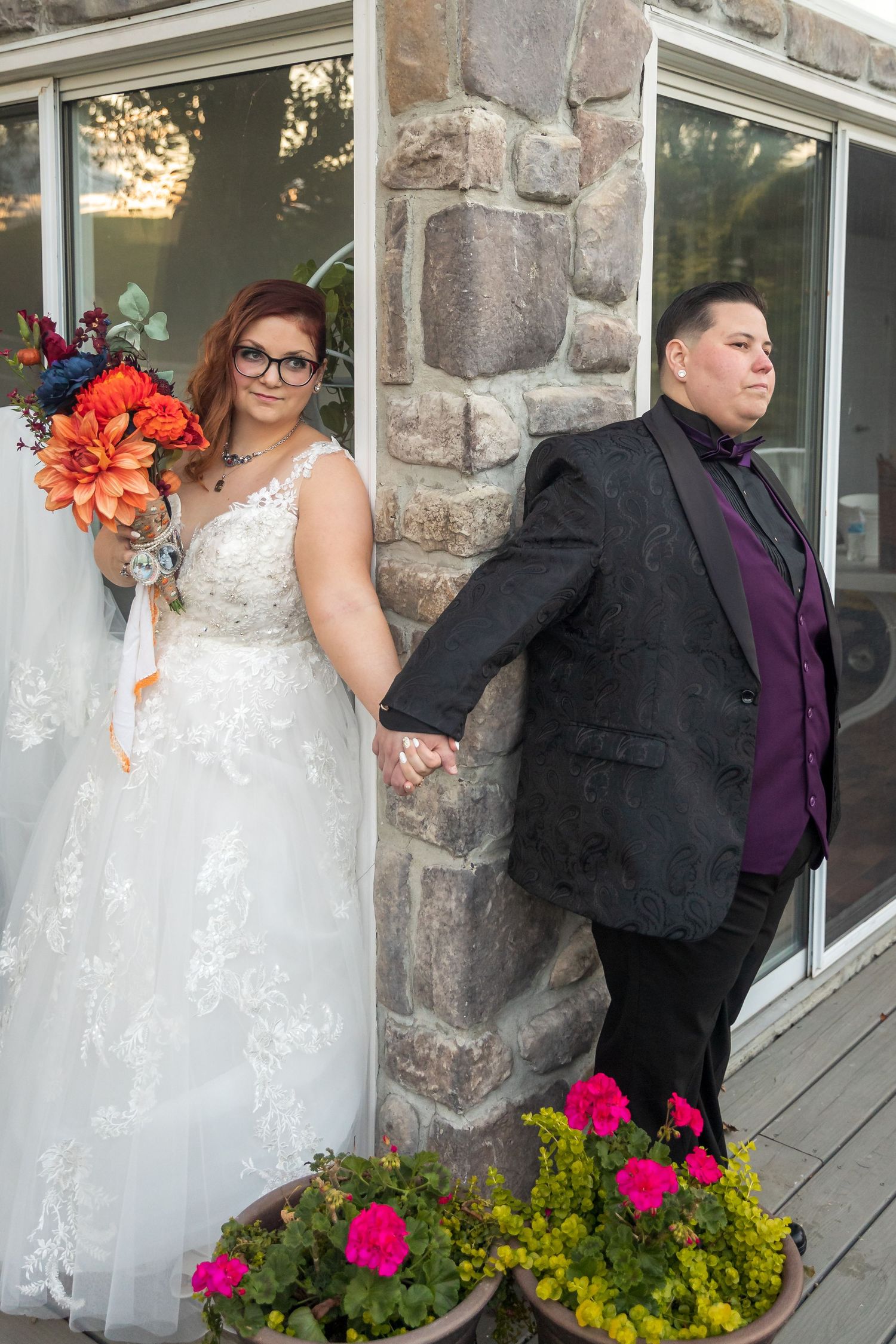Frederick Maryland Wedding Photographer -  Wedding couple poses for photos against stone wall with pink and yellow flowers in foreground.