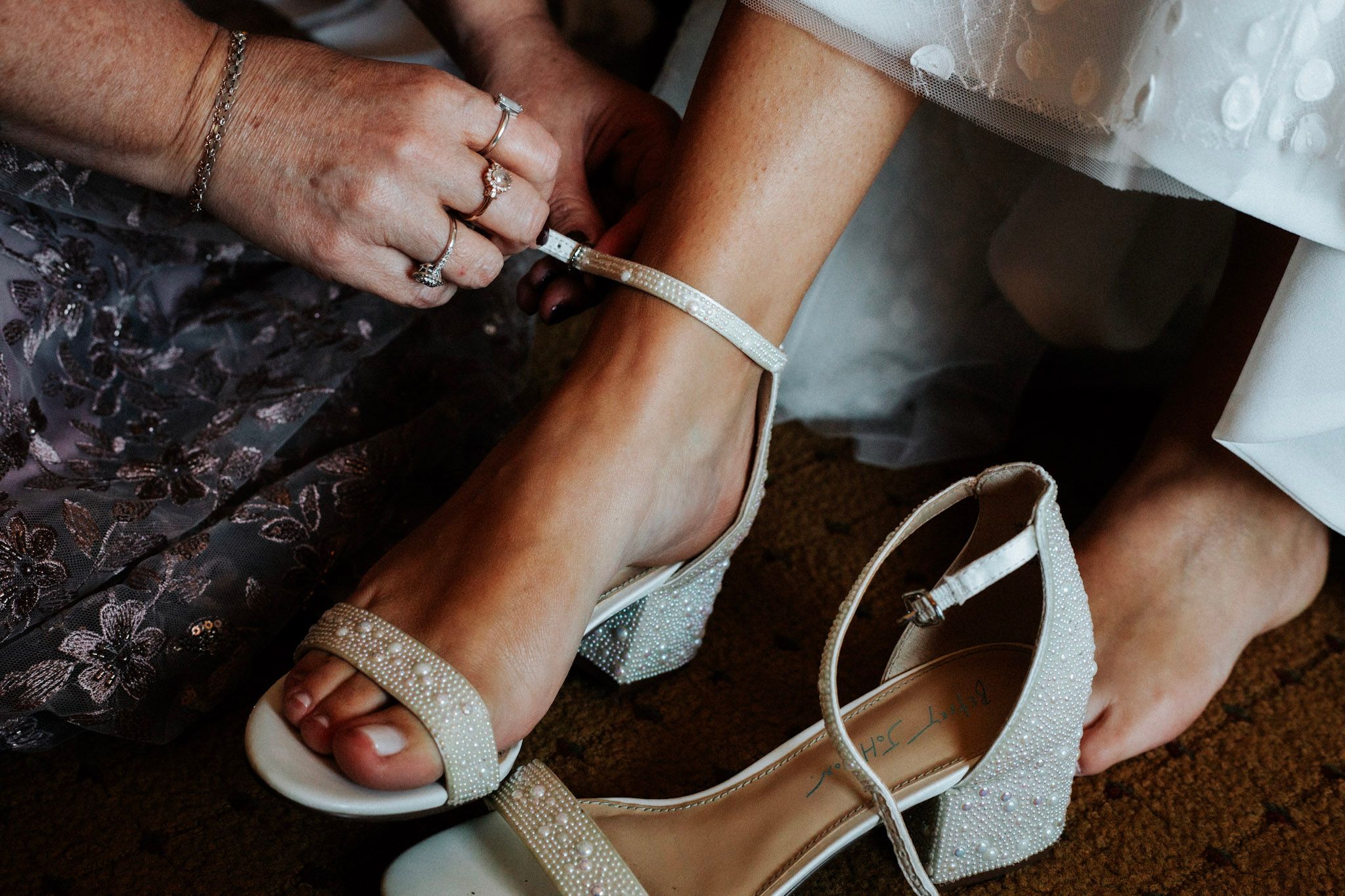 Bride getting strappy white block heel wedding shoes fastened before the ceremony.