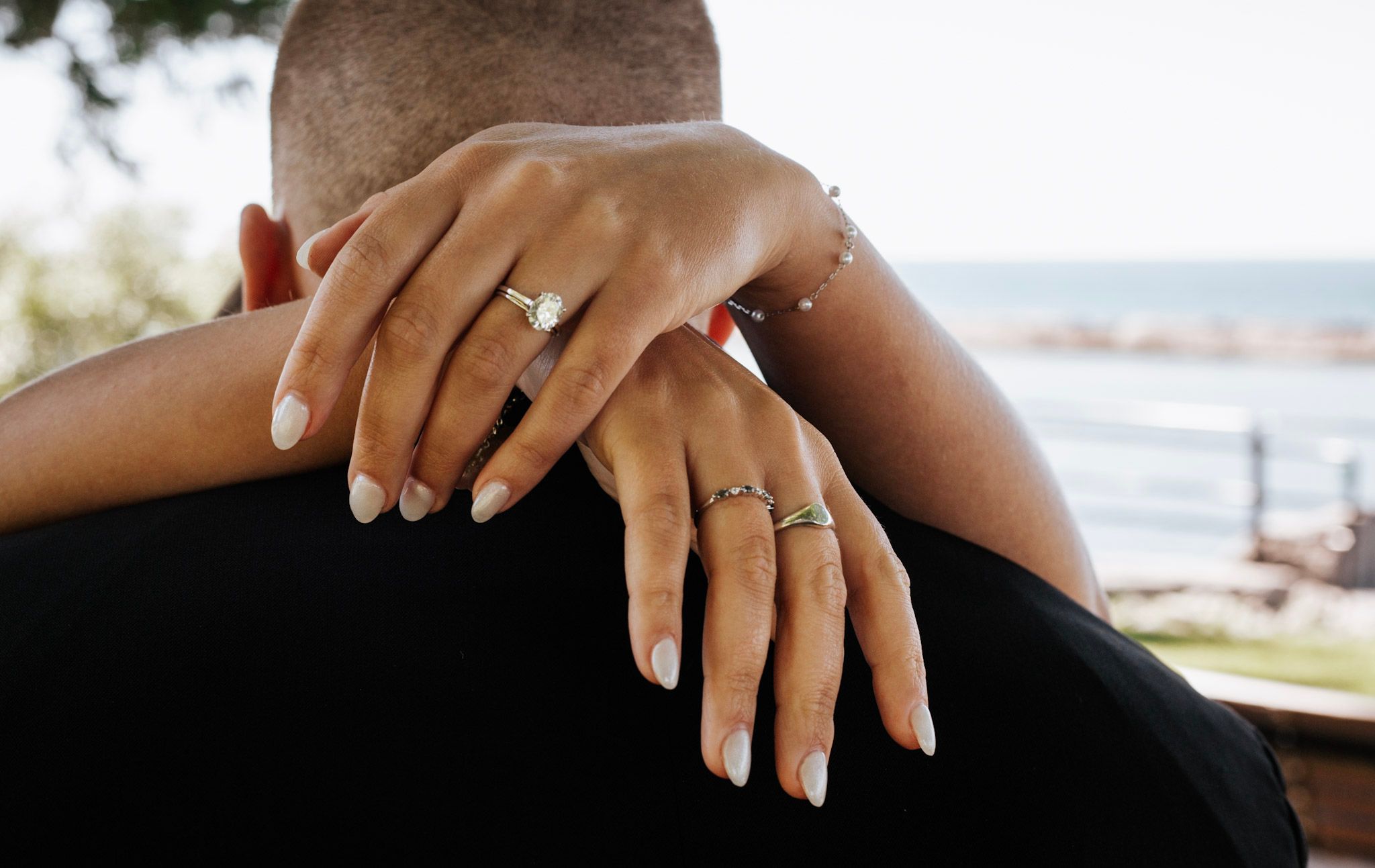 Close-up of engaged couple embracing with diamond engagement ring and wedding band visible.