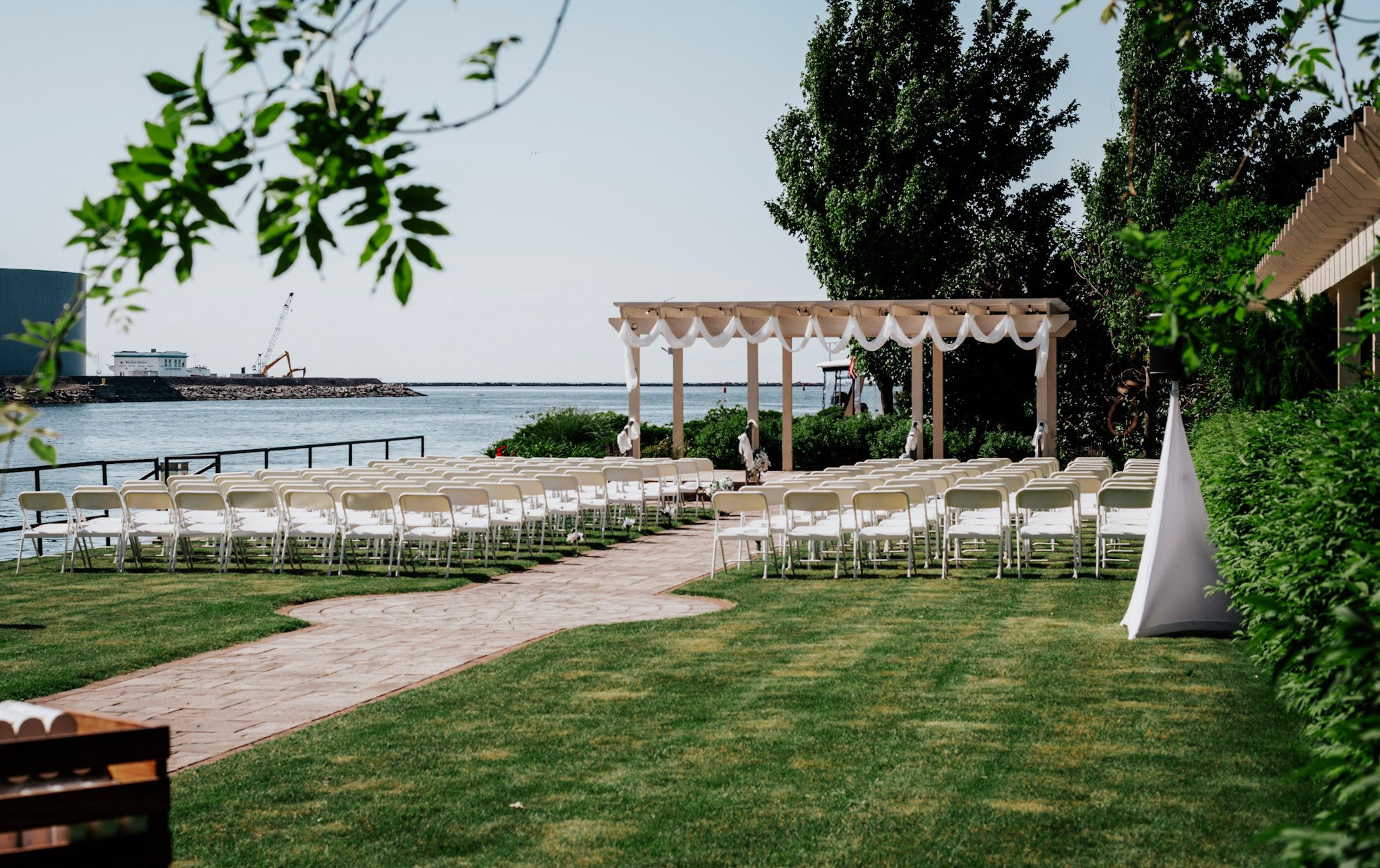 An elegant outdoor wedding ceremony setup with white chairs and a pergola overlooking a waterfront.