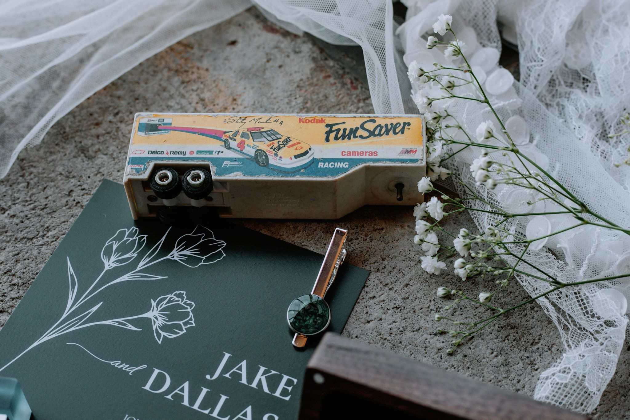 A FunSaver disposable camera rests on a dark wedding stationery book beside flowers and a pen.