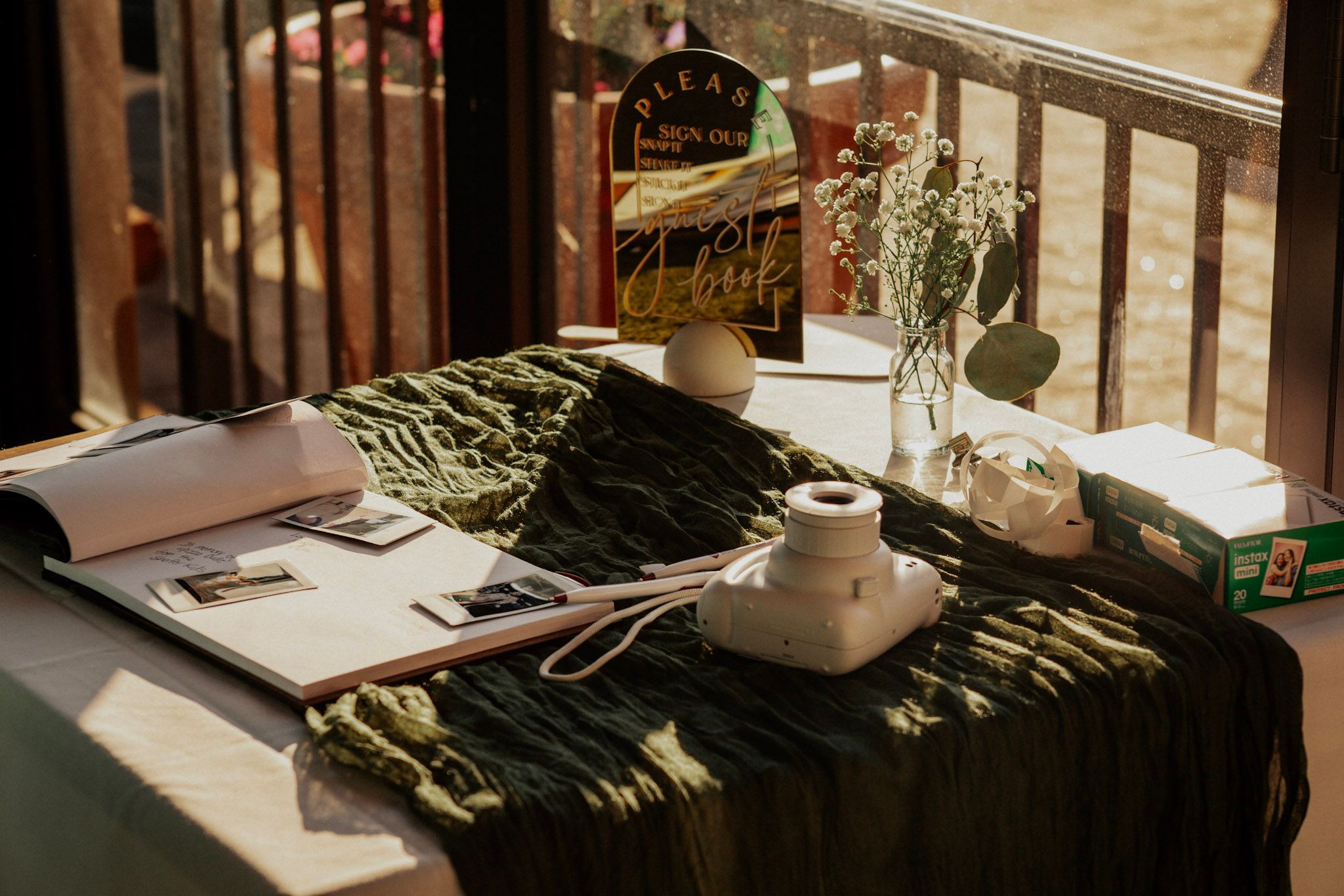 Rustic table with open book, green cloth, small vase of flowers, and vintage items on a balcony.