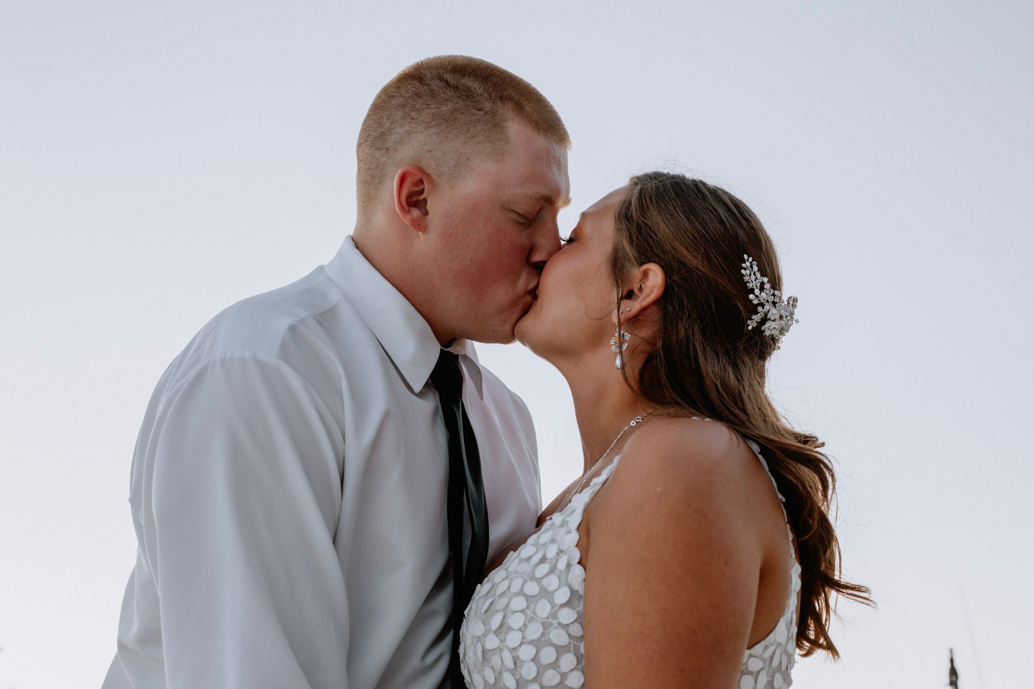 Bride and groom sharing a romantic kiss at sunset during their wedding day.