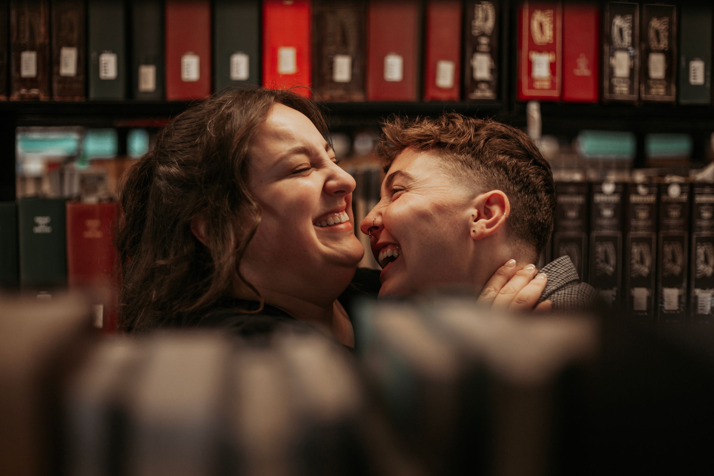 Two people laughing joyfully together between bookshelves in a library or bookstore.
