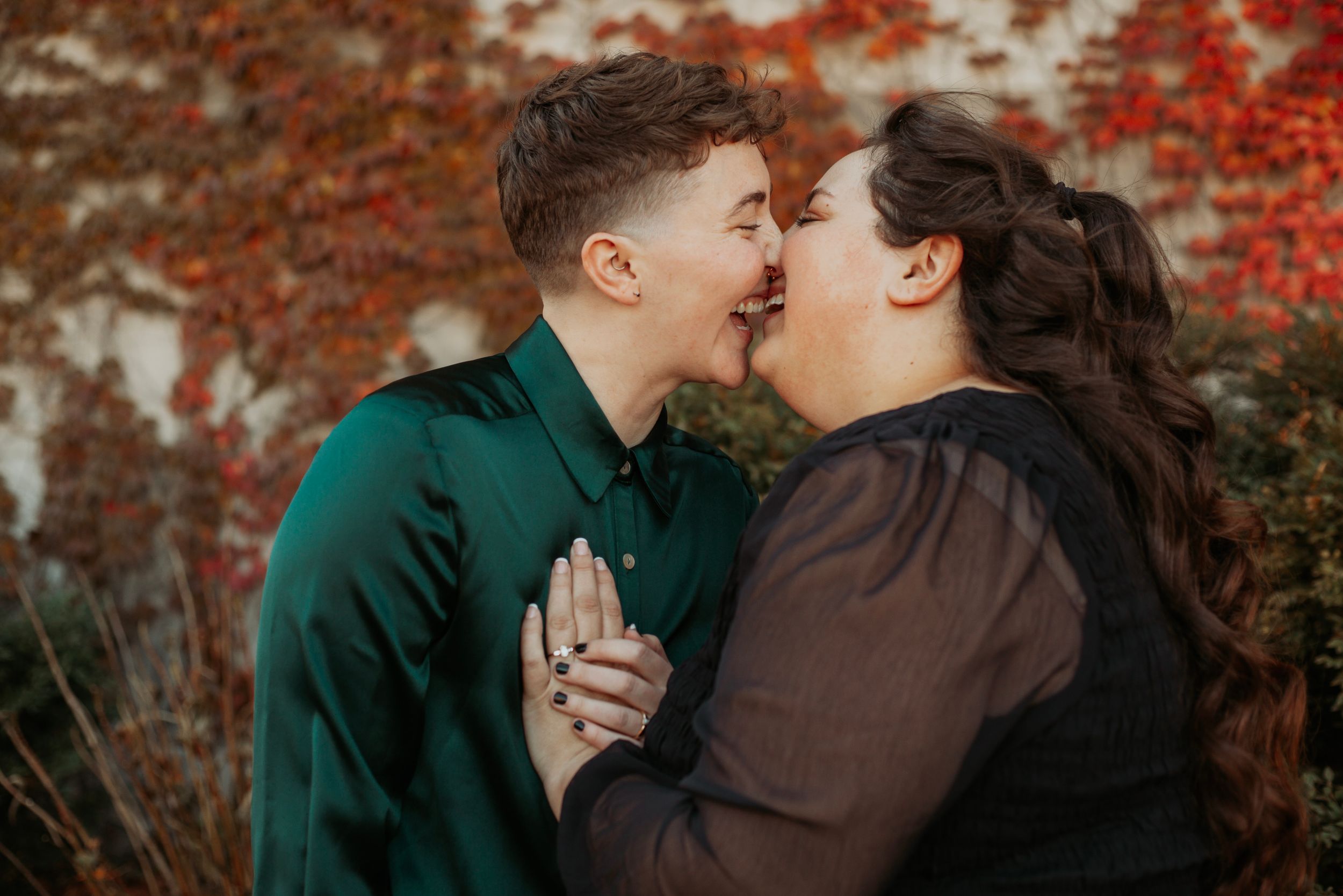 Couple sharing a kiss in front of vibrant red autumn ivy leaves outdoors.