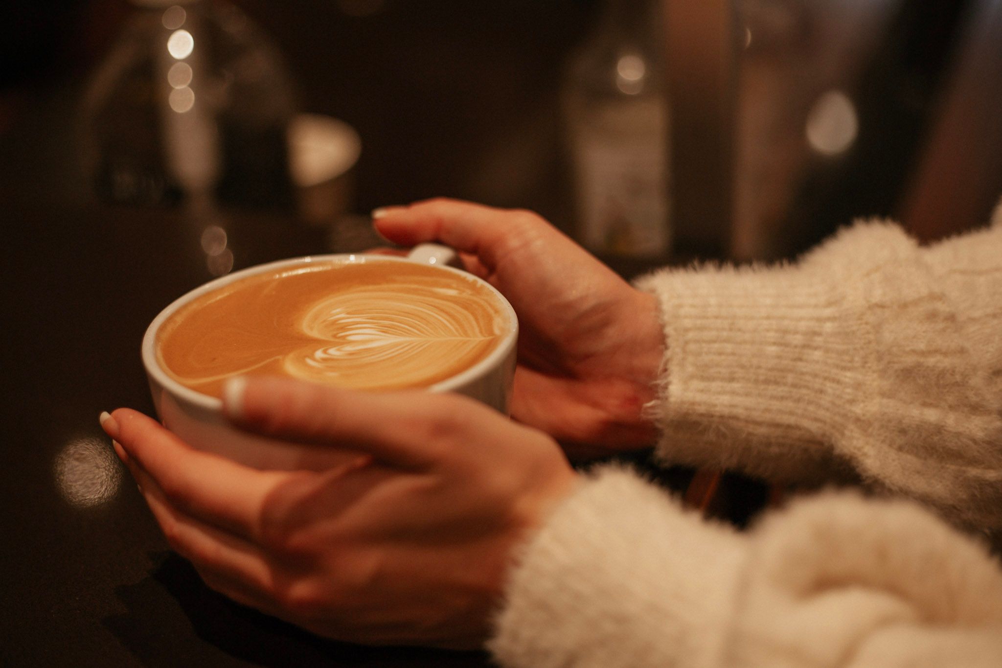 Close-up of hands holding a warm latte art coffee cup in a cozy café setting.