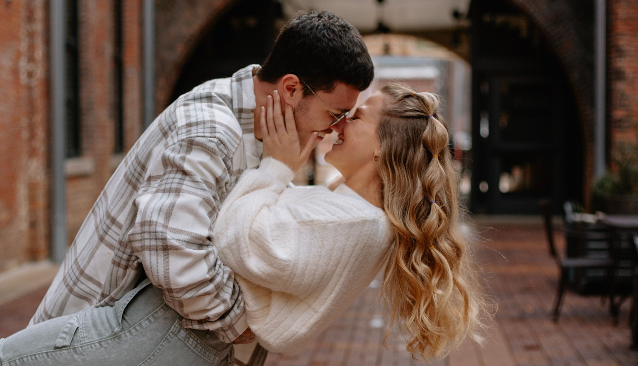 Couple sharing a tender kiss in a charming brick courtyard during engagement photos.