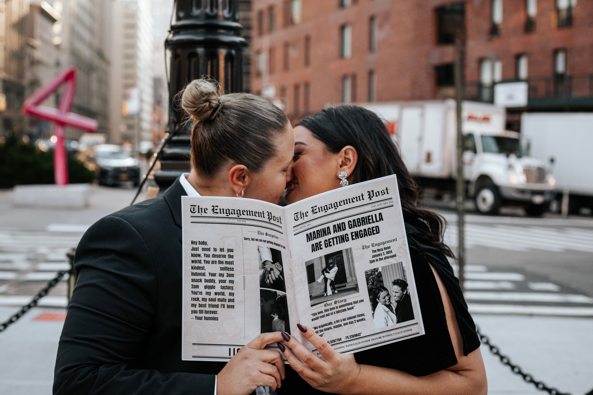 Couple sharing a kiss behind a custom engagement newspaper on a New York City street.