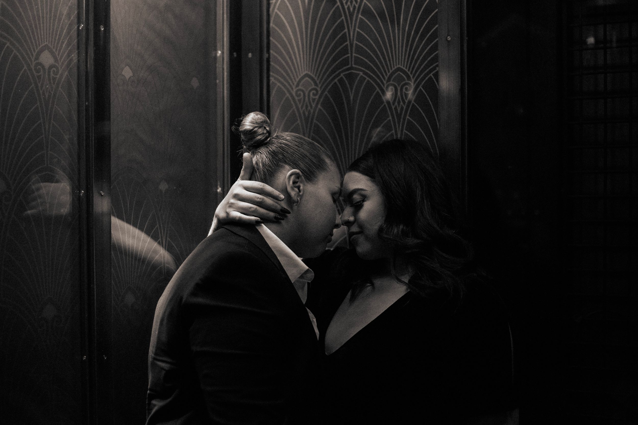 Romantic black and white photo of couple sharing an intimate moment in front of art deco doors.