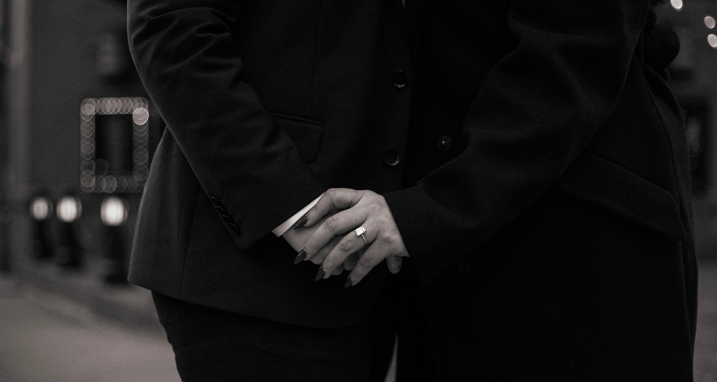 Close-up black and white photo of hands clasped together wearing a ring.
