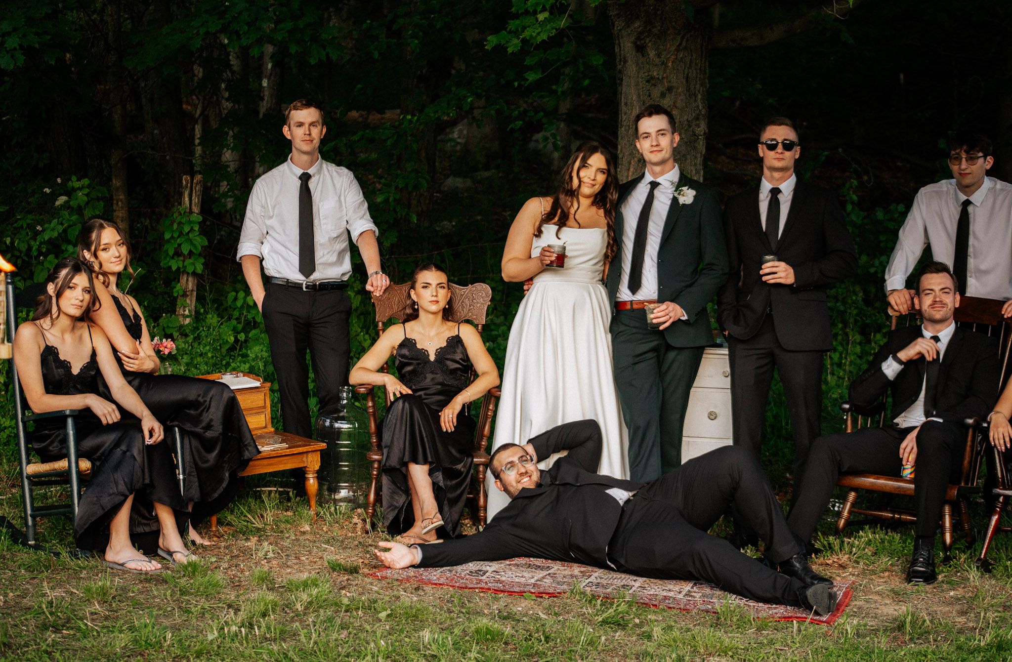 A wedding party poses dramatically in a forest setting with the bride and groom at center.