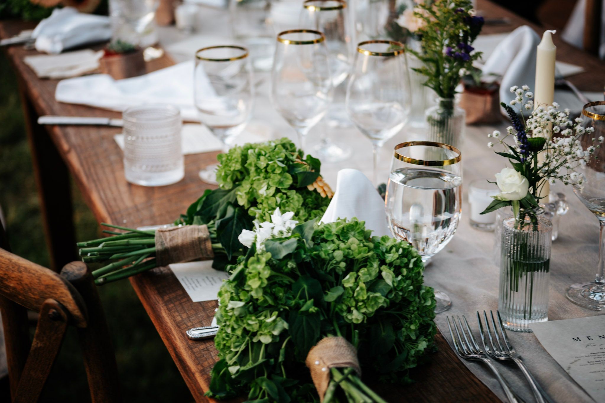 Elegant rustic wedding reception table with green hydrangea bouquets and gold-rimmed glasses.