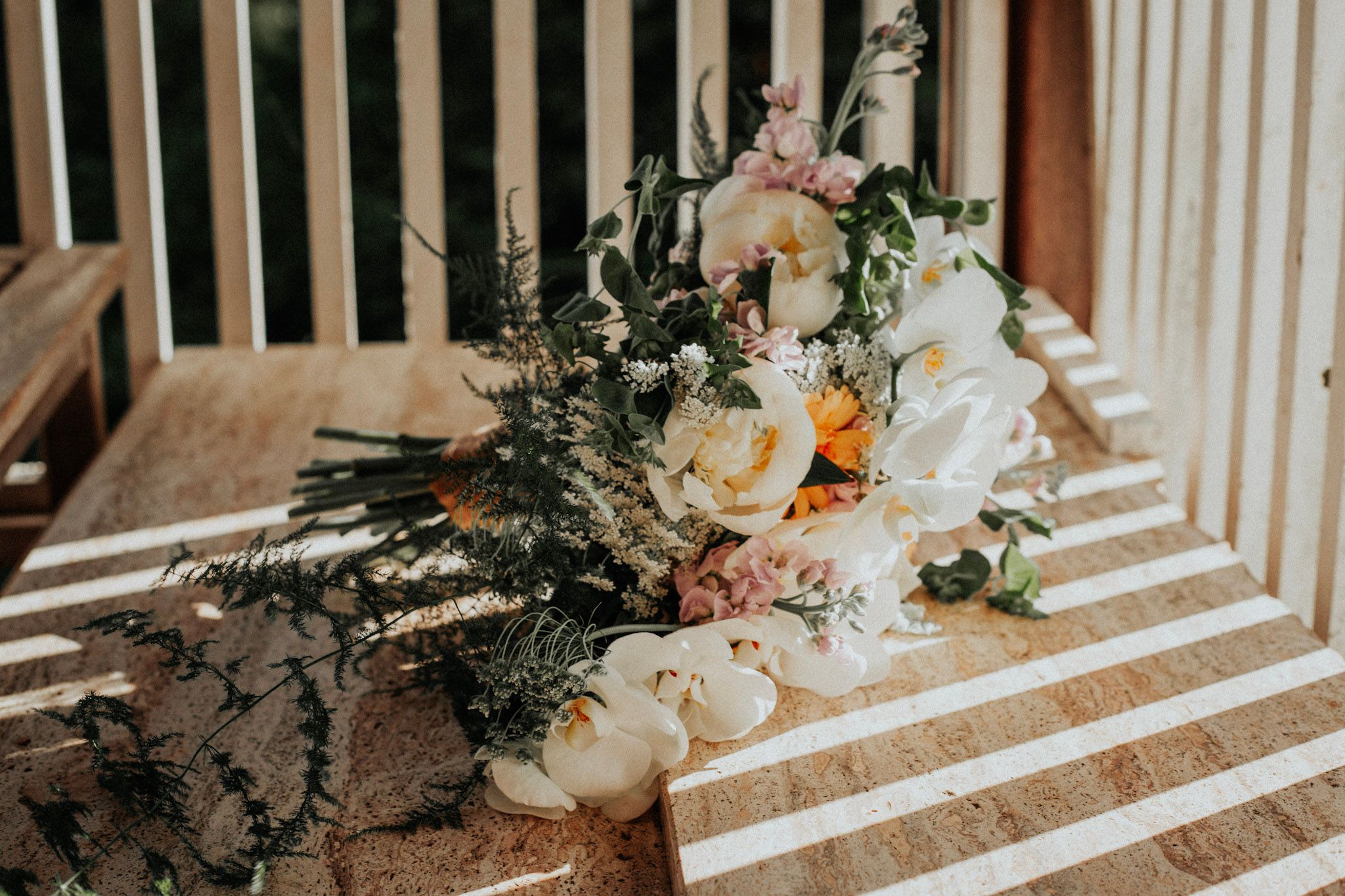 Bridal bouquet with white orchids, peonies, and greenery resting on a striped surface.
