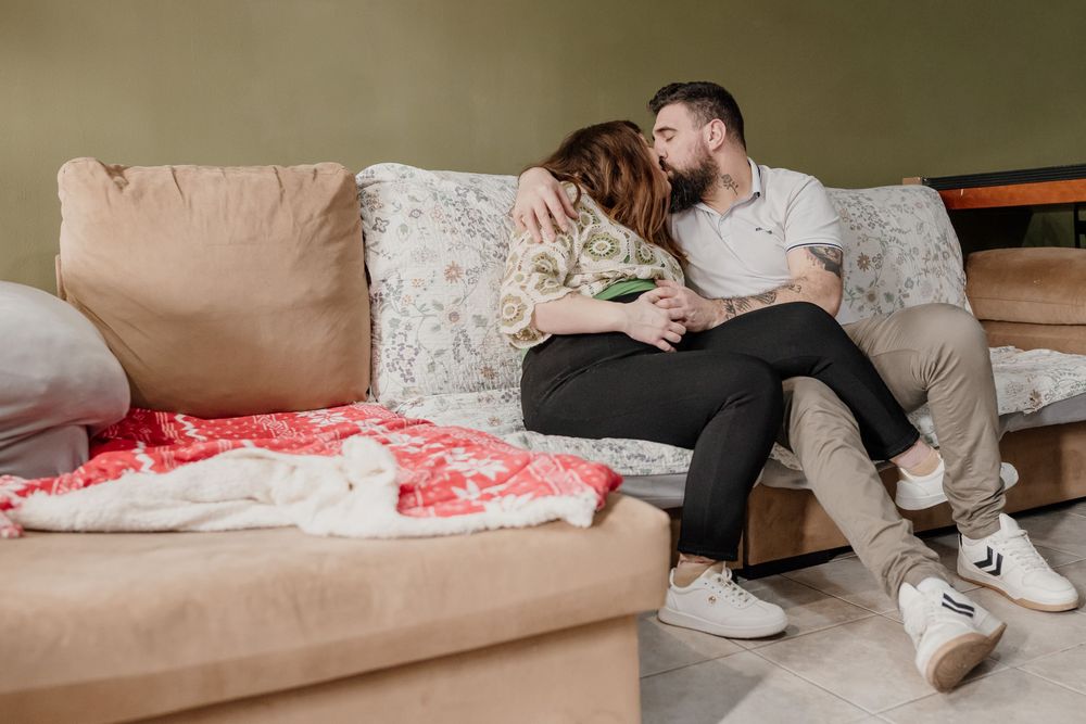 A couple relaxes together on a comfortable beige couch in a cozy living room setting.