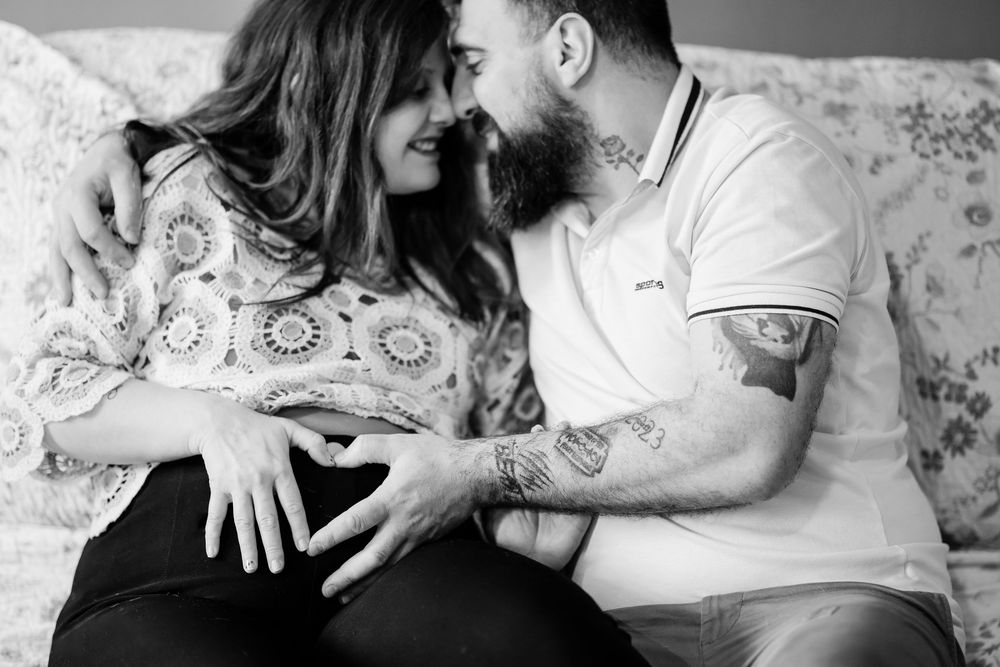 Black and white intimate portrait of an expecting couple sharing a tender moment on a couch.