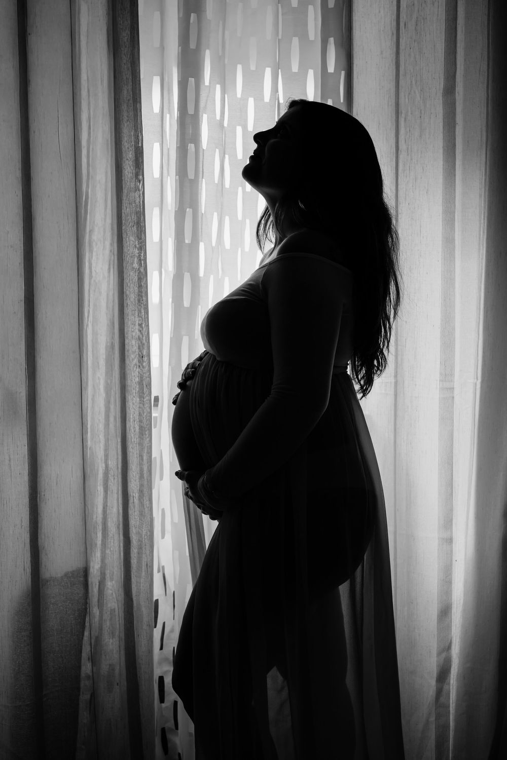 Dramatic black and white silhouettes of people standing against a curtained window with bright backlighting.