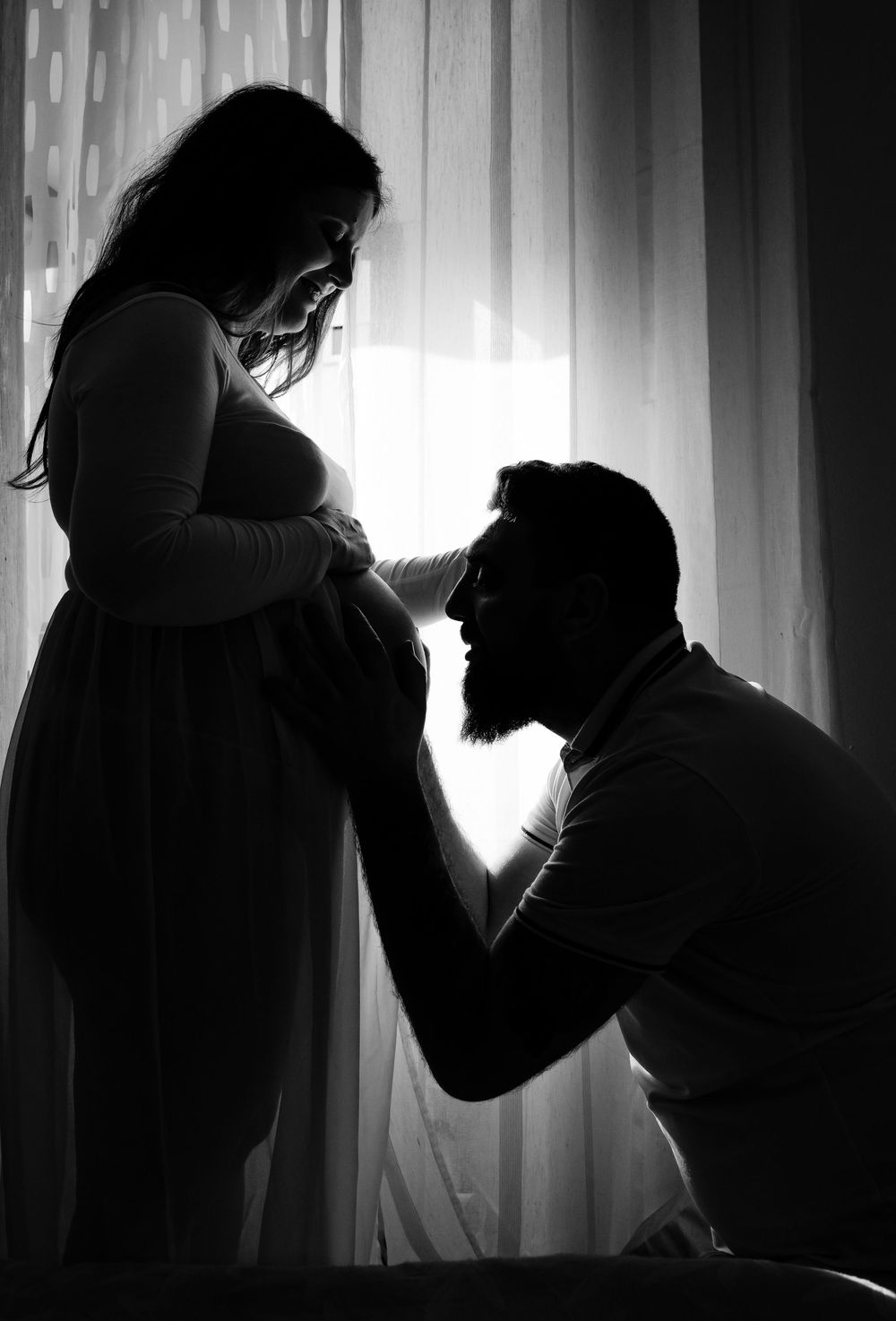 Dramatic black and white silhouettes show a couple dancing in a backlit window with curtains.