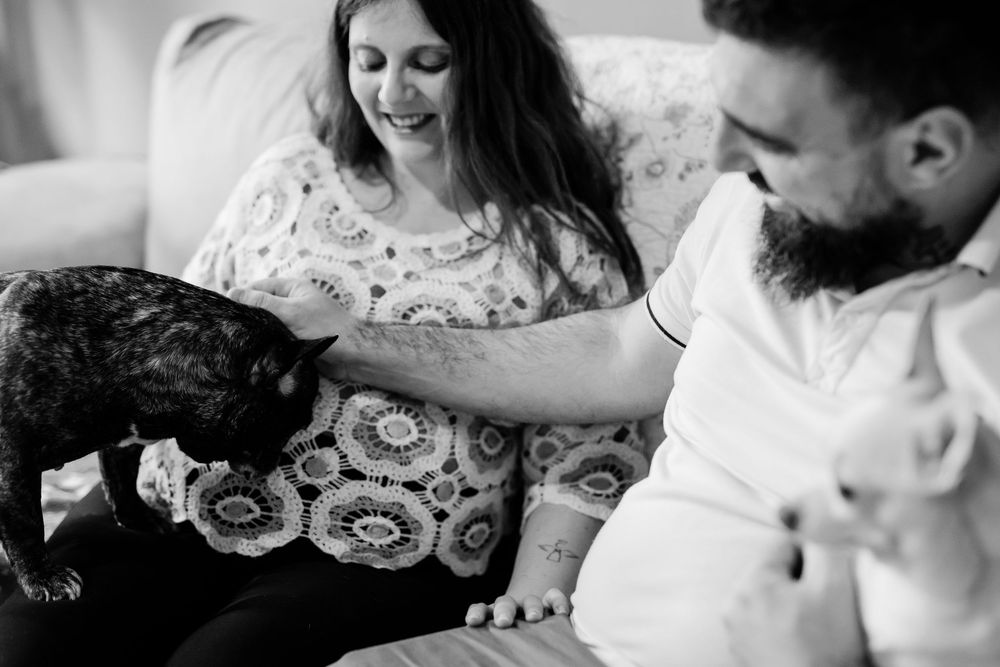 Black and white photo of a couple sitting on a couch petting their black cat in a relaxed, intimate moment.