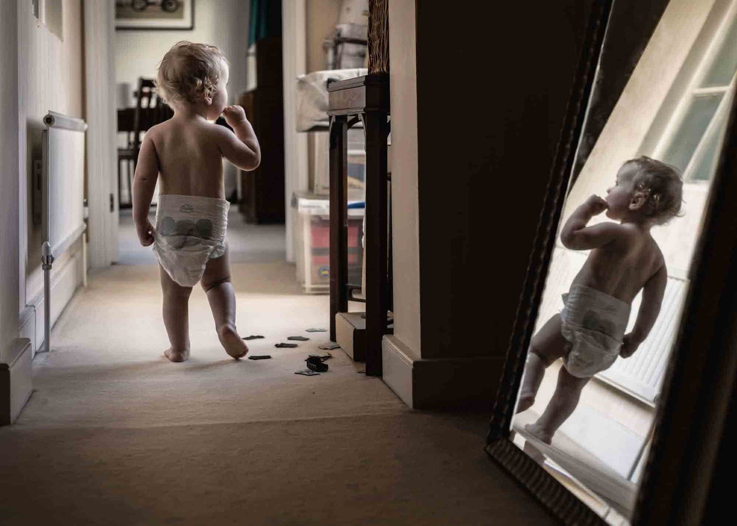 A toddler wearing only a nappy walks down a corridor at an in-home session near Marlow.