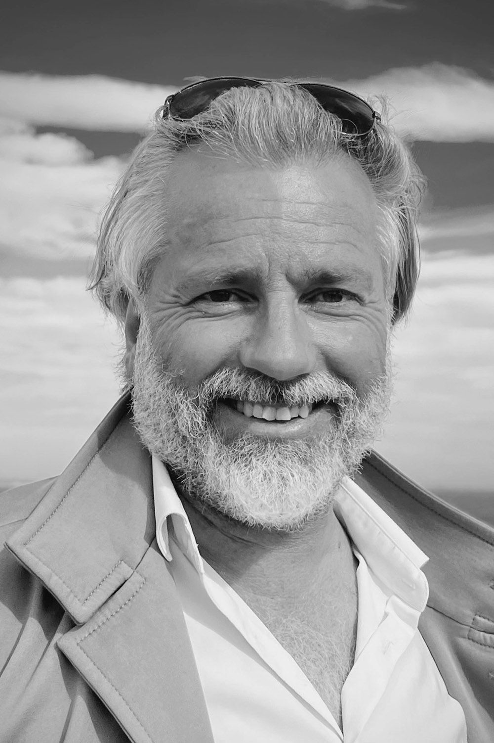Black and white portrait of a smiling bearded person wearing sunglasses outdoors.