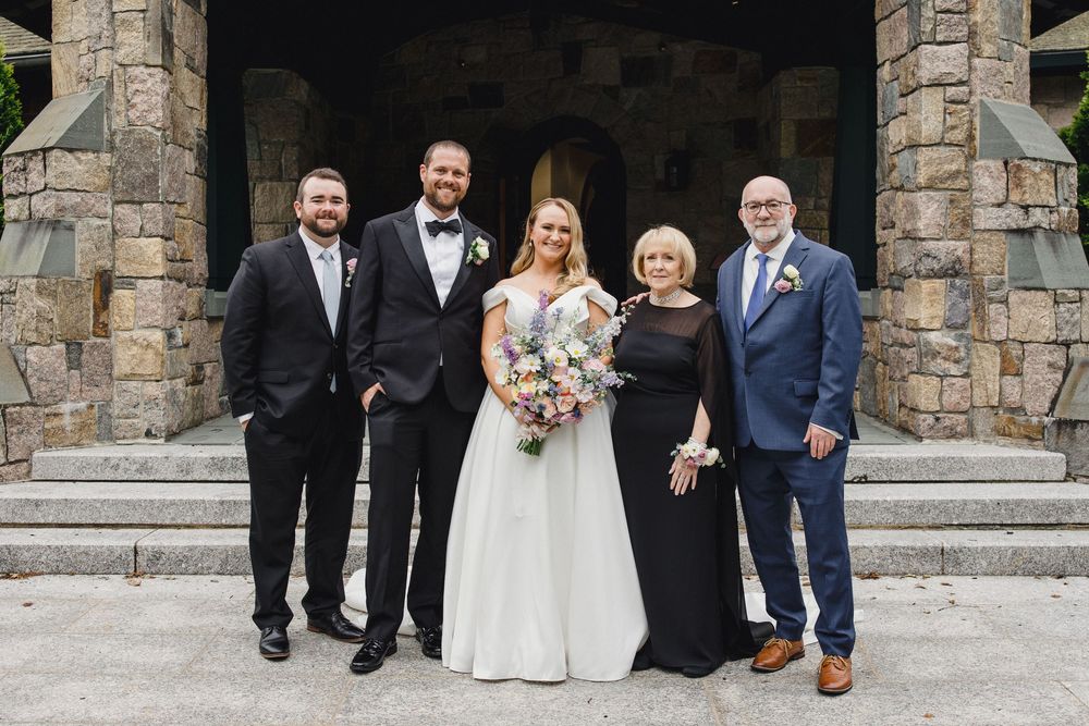 Wedding party members walk together outside a stone building entrance during a formal celebration.