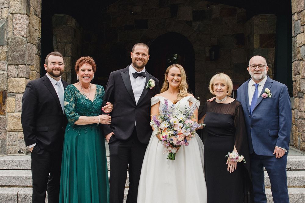 Wedding party poses together in front of stone wall wearing emerald green and formal attire.